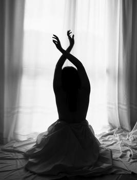 A girl back with hands up, part of a white background of white sheets and curtain.