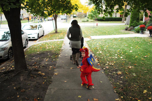 Little boy dressed up as a Dragon for Halloween following his mum down the side walk. He\'s looking back