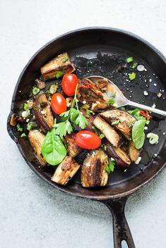 Still life of fried aubergines with plum tomatoes in frying pan