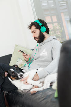 Dog lying besides man listening music through mobile phone at cafeteria
