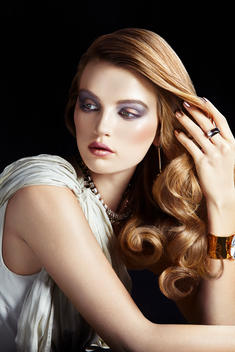 Young caucasian woman with long brunette very groomed wavy hear, wearing high end jewelries and looking over her shoulder
