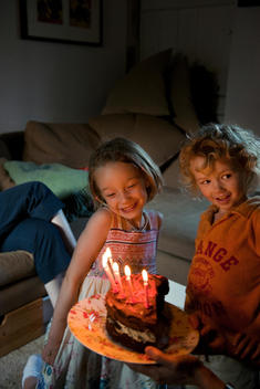 Two young children looking at a part eaten birthday cake with the candles still alight
