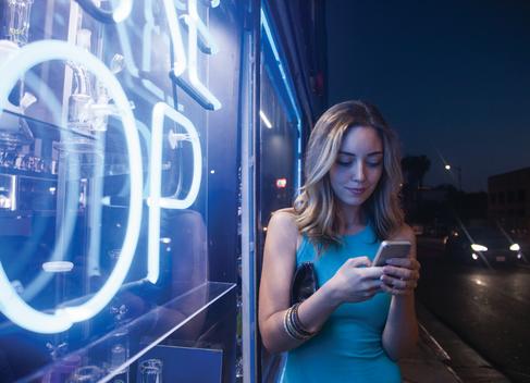Girl by neon lights looking at smart Phone.