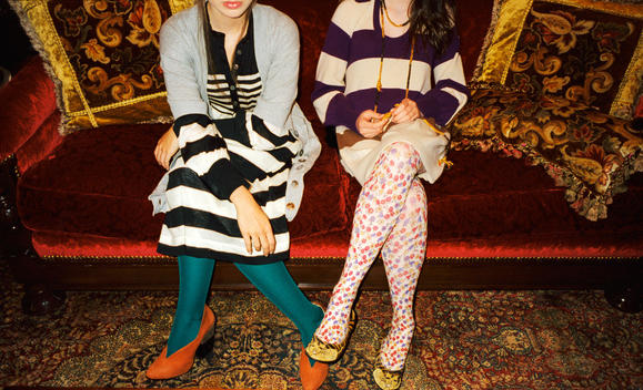2 girls wearing tsumori chisato clothing sitting on couch with ornate pillows and rug