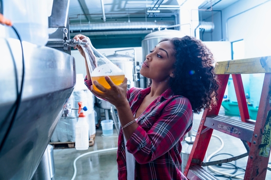Young woman in brewery filling flask with beer from fermentation tank