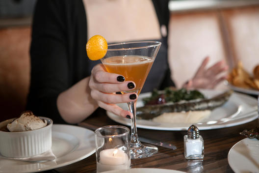 A woman enjoys a cocktail with her dinner at a nice restaurant.