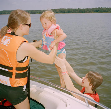 A teenage boy hands his aunt, a young mother, her daughter over the stern of a boat on Lake Tyler where their family\'s lake house is located. Tyler, Texas