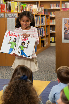 Mixed race girl showing Spanish book to classmates in library