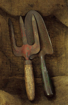 Close up from above of well-used garden trowel and hand fork lying on hessian sack