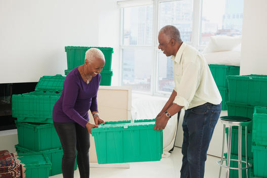Older Black couple carrying boxes in new home