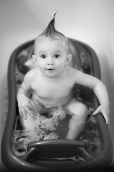 Portrait of a toddler playing in a baby bath tub with bubbles and soap in her funny hair style.