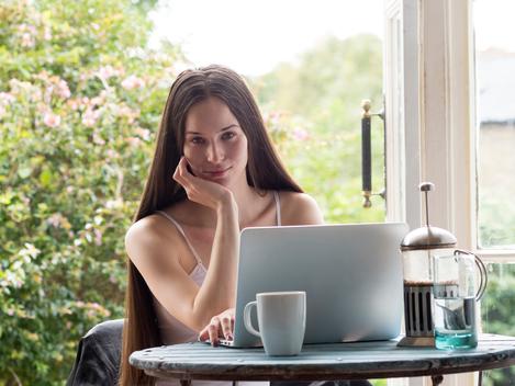 Portrait of young woman sitting at table, coffee and laptop in front of her