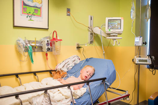 Grant, a young red-head boy, lies in the hospital bed with tubes connected to his body and teddy bear nearby after nearly drowning in the pool before his mother pulled him out of the water. Heritage Hills, Colorado