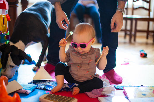 A baby plays the xylophone while wearing pink heart shaped sunglasses.