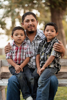 Hispanic father and sons sitting on park bench
