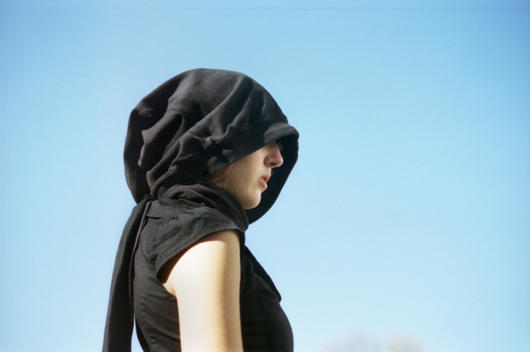 A Young Girl With Her Face Hidden Behind A Solid Black Veil.