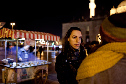 Young Turkish women are chatting in the Eminonu Square where famous New Mosque is located behind themselves and there is a street vendor selling chestnut from his cart at the night moments from Istanbul.
