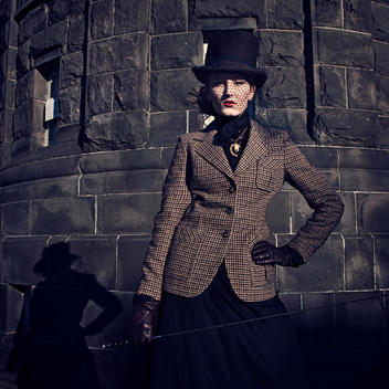 Female young adult in period clothing wearing black hat and veil with Harris tweed jacket and gloves holding riding crop looking at camera