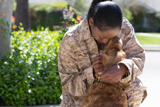 Female soldier hugging pet dog on street at homecoming