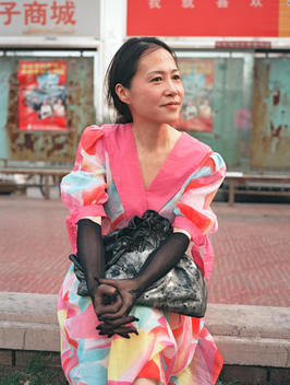 Woman sitting on a bench wearing a colorful dress and black gloves in the Haidian district of Beijing, China, 2005.