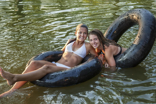 Two girls swimming and floating using swim floats and inflated tyres.