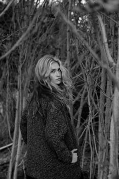 A beautiful blonde women in a coat, walking in the woods.