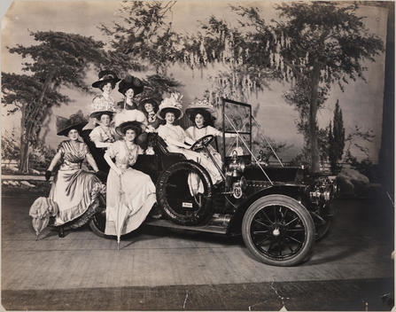 Group Portrait Of Chorus Girls Posing In A Studebaker On What Appears To Be A Stage With A Painted Backdrop.