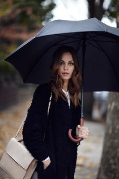 Girl on sidewalk in black coat with umbrella