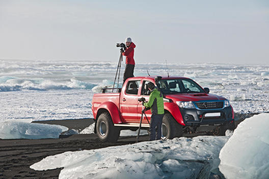 Photographer on top of off road vehicle on iceberg beach, Jokulsarlon, South East Iceland, Iceland