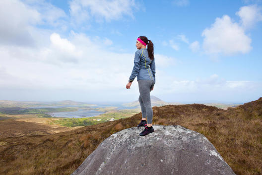 Young athletic women standing on rock in mountainous terrain contemplating run