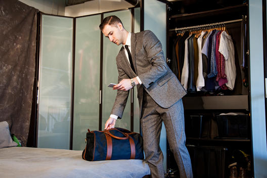 Man in suit packing duffle bag while using phone.