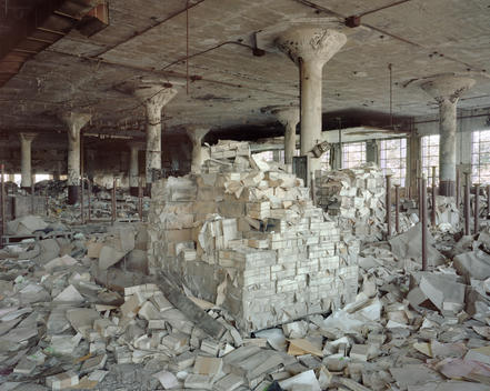 Large pale pile school report cards resting in an abandoned factory floor surrounded in piles of scattered papers and forms.