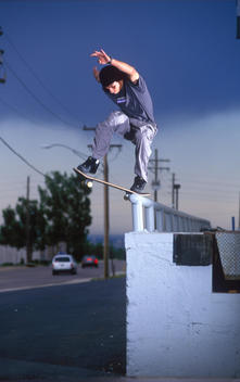A skateboarder doing a trick (backside nose blunt slide) on a blue handrail mounted on top of a high loading dock.