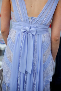 The back of a woman wearing a blue/purple dress with a bow and lace.