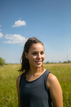 A portrait of a beautiful girl in athletic wear standing in a sunny field.
