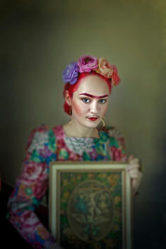 Young woman with flowers in her hair holding painting looking at camera