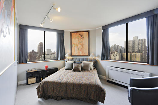 Bedroom With Bed Placed Diagonally Between Picture Windows With Views Of City