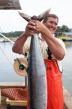 a fisherman smiling and holding up a large fish on his boat