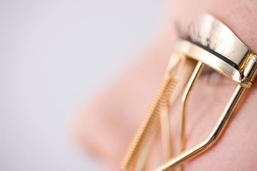 Close up of young woman curling eyelashes with eyelash curler