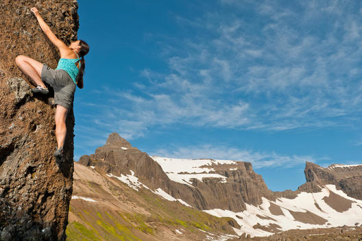 Female climber scaling steep rock with Dyrfjoll at the horizon, East Iceland, Iceland