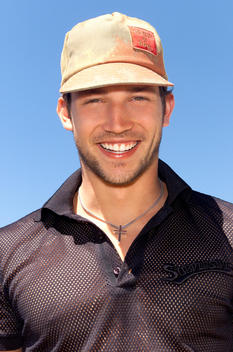 Young man in mesh shirt and baseball cap.