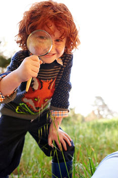 boy with red curly hair looking trough a magnifier lens smiling