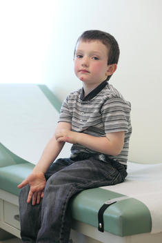 Boy Sitting On Doctors Check Up Table