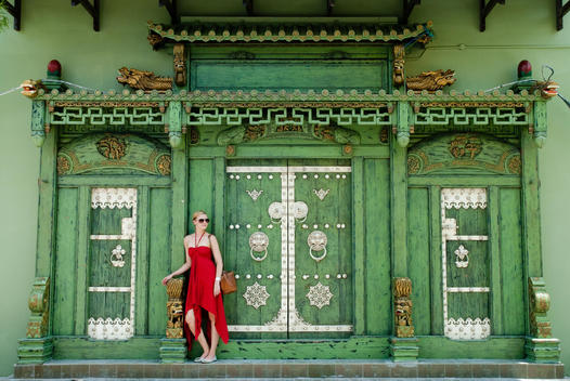Tourist In Red Long Dress Standing In Front Of The Back Door Of A Chinese Temple In Colonial Georgetown.