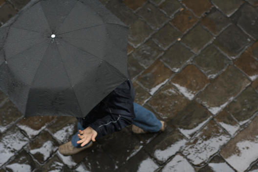 Overhead view of a person walking with an umbrella with their hand sticking out from under the rainbow