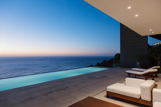 Modern patio and infinity pool overlooking ocean at sunset