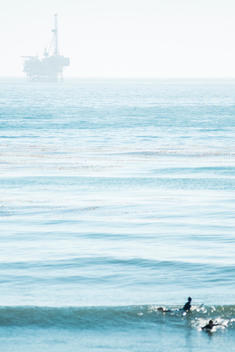 surfers paddling for wave with in the pacific ocean with oil rig in the background.