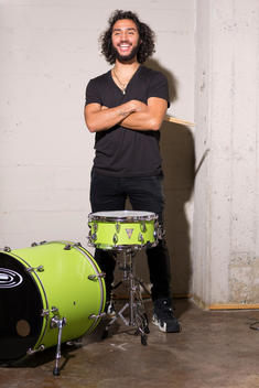 Mixed ethnicity Millennial man standing loft playing green drum set.