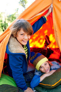 two boys peeking from their mounted camping tent smiling and laughing