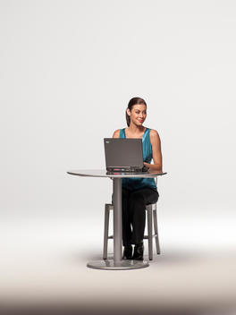 Young woman sits alone at small round table working on lap top computer